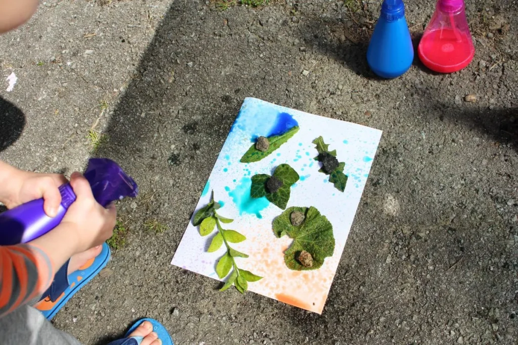 A close up of a child spraying a paper covered in leaves.