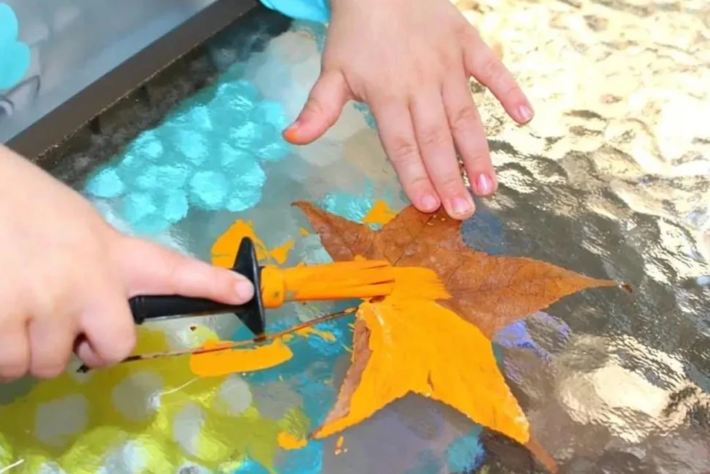 A child using a paintbrush to paint a brown leaf bright orange.