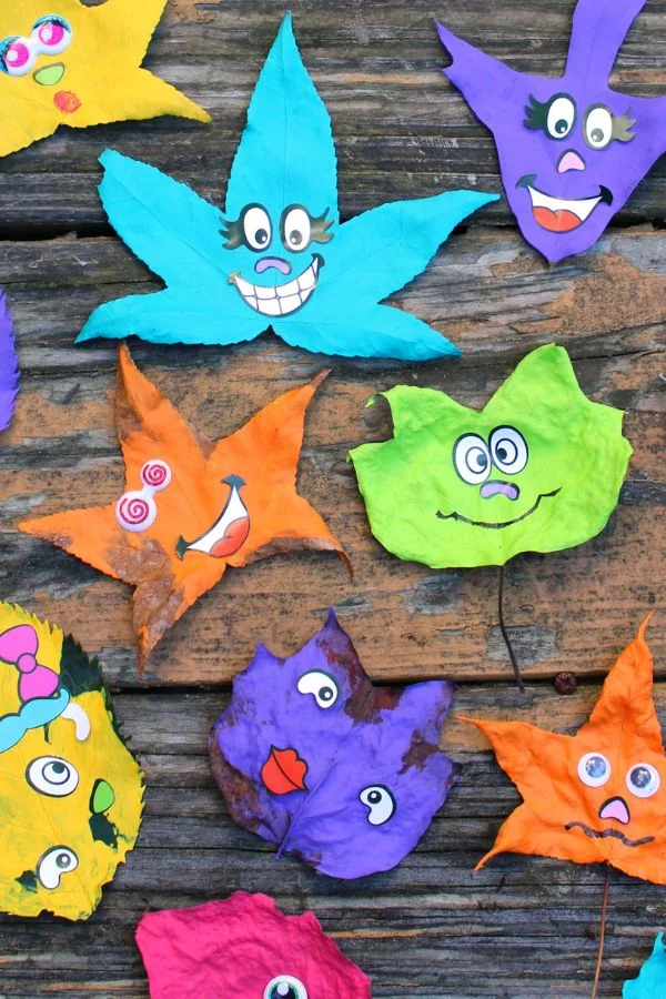 A collection of painted leaves with silly faces laying on a wodden table. 