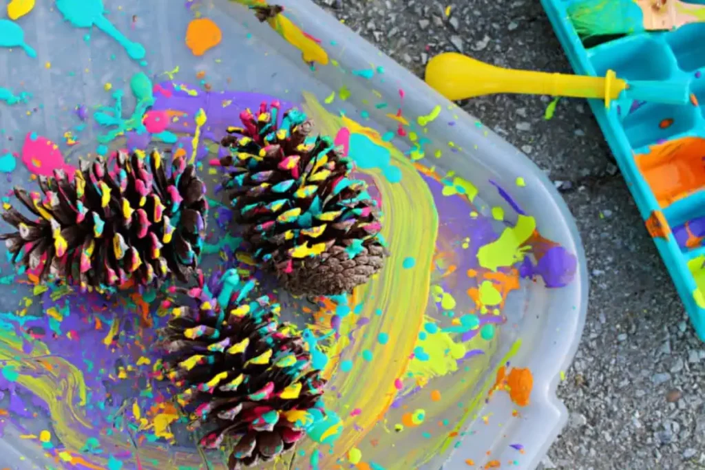 3 painted pine cones on a tray next to an ice cube tray full of different color paints.